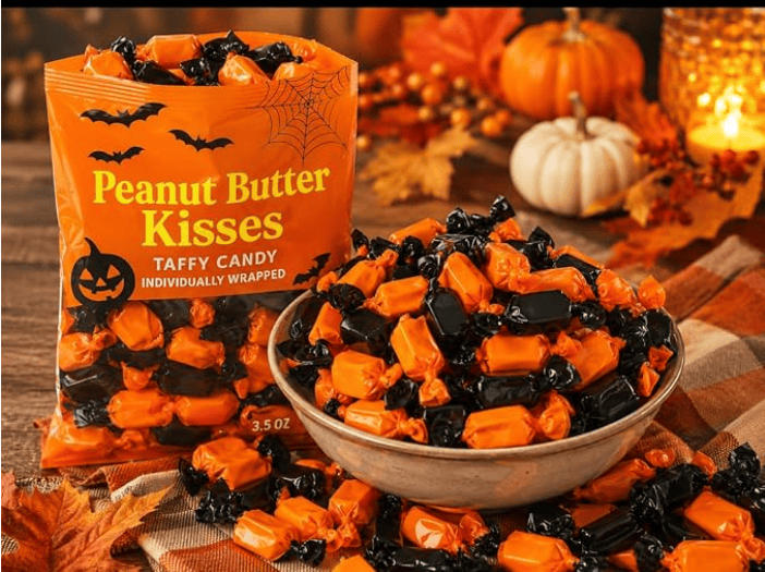 A bag of Peanut Butter Kisses taffy candy in Halloween-themed orange and black wrappers, displayed next to a bowl overflowing with the candies. Fall decor with pumpkins and leaves is in the background.